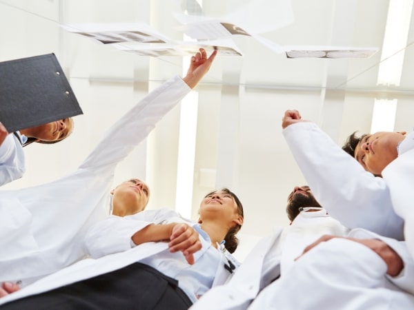 Un gruppo di giovani in camice bianco discute intorno a un tavolo, rappresentando l'apprendistato di alta formazione nel campo della ricerca