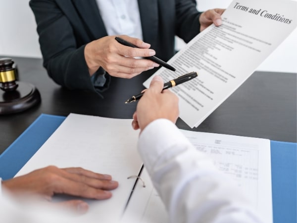 un consulente del lavoro e un cliente parlano durante una consulenza buste paga, con documenti e una penna in primo piano.