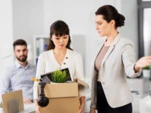  una donna viene accompagnata da un'altra, probabilmente la sua supervisore, mentre lascia l'ufficio portando una scatola con i suoi effetti personali, in seguito al suo licenziamento