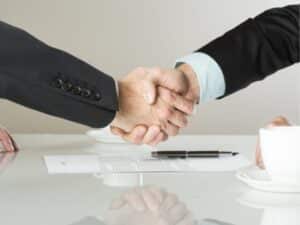 Due uomini d'affari che si stringono la mano sopra un tavolo, con documenti di contratto prestazione di servizi professionali, egno di un accordo raggiunto.