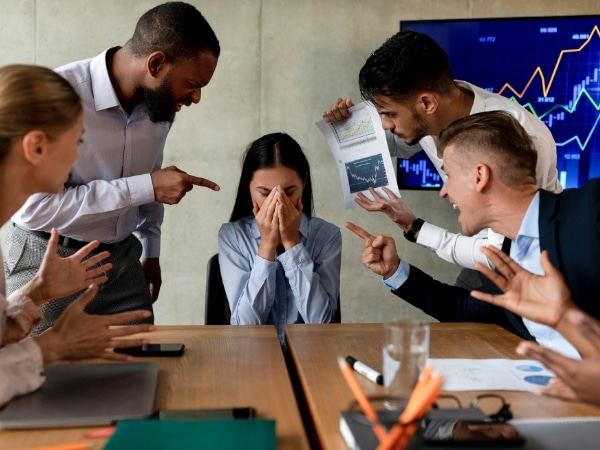 Una dipendente è in lacrime mentre viene accusata da più colleghi in una riunione. Rappresentazione di una scena di mobbing.