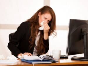 ragazza in ufficio con fazzoletti e raffreddore, simbolo di una malattia comune e non professionale