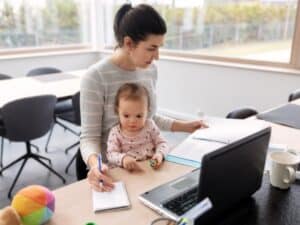 mamma lavoratrice, seduta a un tavolo con suo figlio piccolo, gestisce documenti e un computer portatile