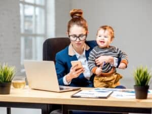 una mamma lavora dietro una scrivania mentre tiene in braccio suo figlio piccolo