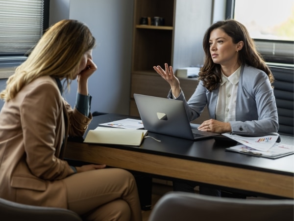 Una lavoratrice è seduta di fronte a una consulente del lavoro in un ufficio, cercando supporto per la denuncia per mobbing.