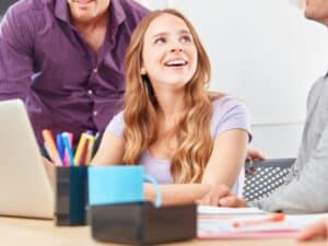 Studente sorridente durante uno stage curriculare, in un ambiente collaborativo con tutor e colleghi.