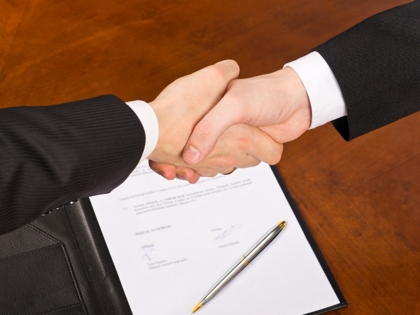Stretta di mano formale tra due persone vestite in giacca sopra un contratto firmato