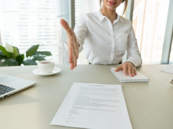 Persona porge la mano per una stretta sopra un documento intitolato 'contratto' su una scrivania